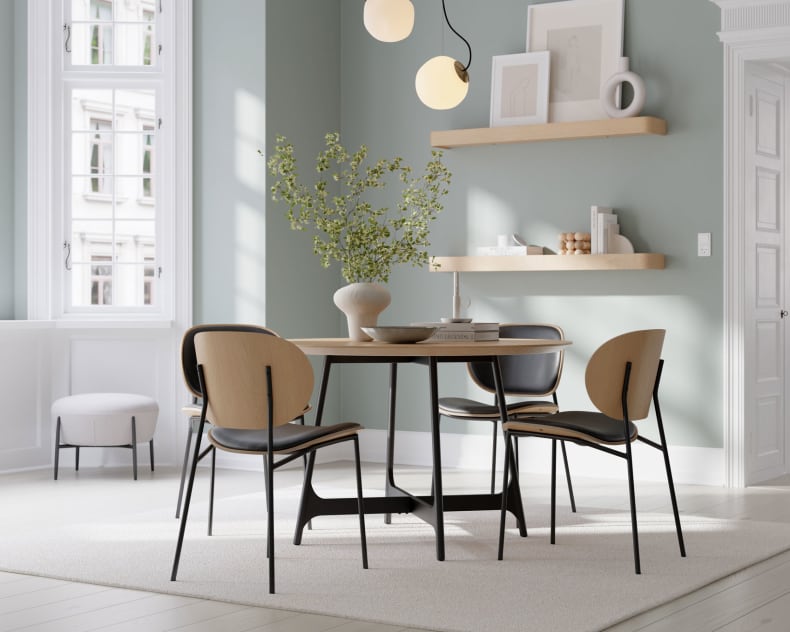 Modernes Esszimmer mit dem runden Tisch Dan Form Tisch Ooid, vier Stühlen, grünen Wänden, Regalen und einer Vase mit Zweigen.