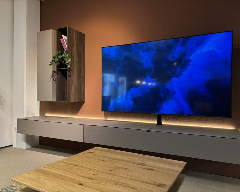 Modernes Wohnzimmer mit einem wandmontierten TV-Gerät auf dem TV-Möbel Next von Spectral, schwebenden Regalen und einem Couchtisch aus Holz.