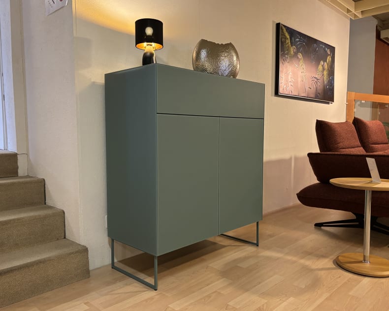 Das Spectral Sideboard 101cm, in modernem Grün, steht neben der Treppe und einem roten Stuhl auf einem Holzboden, gekrönt von einer Lampe und Dekor.
