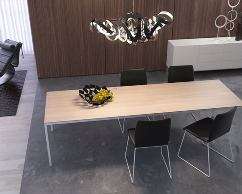 Salle à manger moderne avec la table à manger en bois Willisau Dino, quatre chaises noires et une coupe de fruits sous une lampe sculpturale.