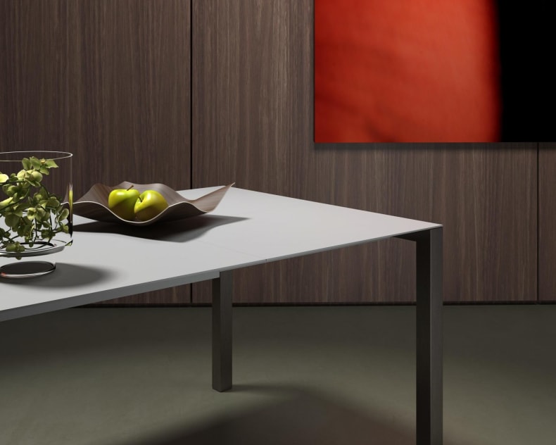 La table à manger minimaliste Willisau Prato, ornée de pommes et d'un vase en verre, se dresse devant des murs lambrissés décorés d'œuvres d'art abstraites rouges.