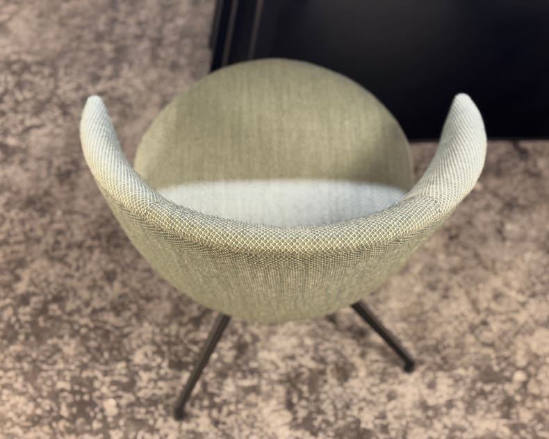 Vue de dessus de la chaise Willisau Loreo (copie), une chaise moderne en tissu vert clair avec des pieds en métal noir, posée sur un sol moucheté.