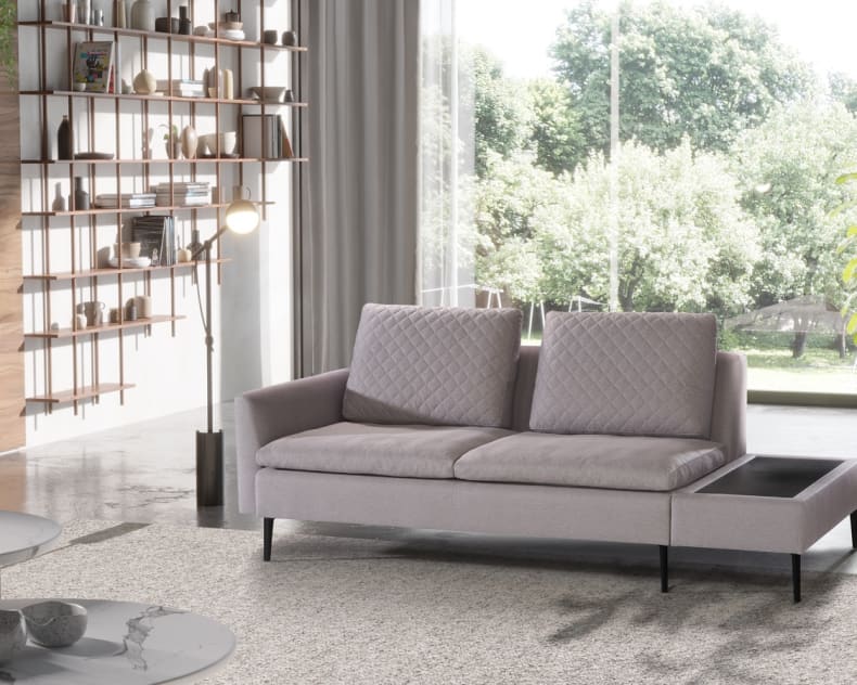 Modernes Wohnzimmer mit dem Artanova Sofa Dyo 9192 in Hellgrau, mit einem großen Fenster, Bücherregalen und einem malerischen Blick ins Grüne.