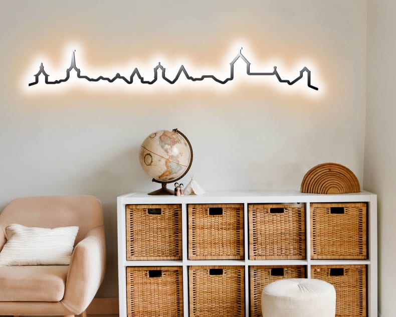 Ein gemütliches Zimmer mit einer Korbablage, einem Globus und der Kontura City Bern leuchtenden Skyline-Wandleuchte über dem Schrank.