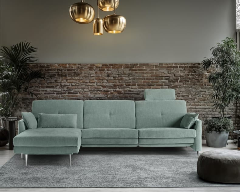 Modernes Wohnzimmer mit dem Horst Sofa Chiasso in Grün, einer Backsteinwand, üppigen Pflanzen, einem grauen Teppich und goldenen Pendelleuchten.