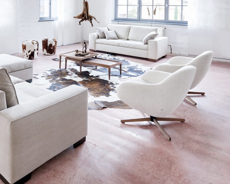 Modernes Wohnzimmer mit Signet Sessel Messina Jester klein, leichten Sofas, Kuhfellteppich, Couchtisch und großen Fenstern.