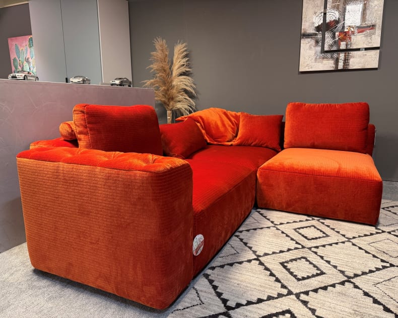 Das Candy Sofa Club House, ein kühnes rotes Sektionssofa aus Samt, steht auf einem gemusterten Teppich in einem modernen Wohnzimmer mit dunklen Wänden.