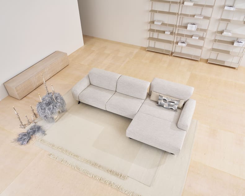 Modernes Wohnzimmer mit dem Himolla Sofa Signa 1552 in Hellgrau, gepaart mit Teppichen, minimalem Dekor und leeren Regalen.