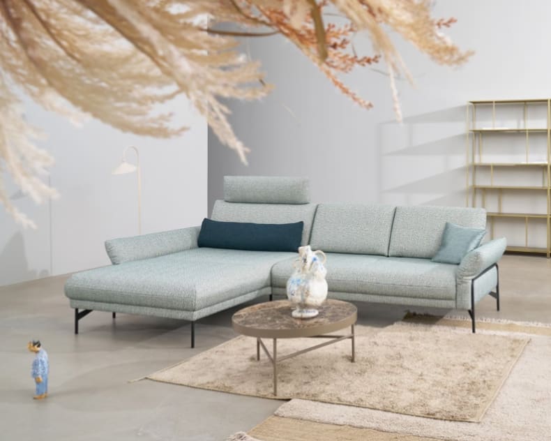 Modernes Wohnzimmer mit dem hellblauen Sektionssofa Himolla Polstergruppe Nova 1370, ergänzt durch einen runden Couchtisch, einen Teppich und ein minimalistisches Dekor.