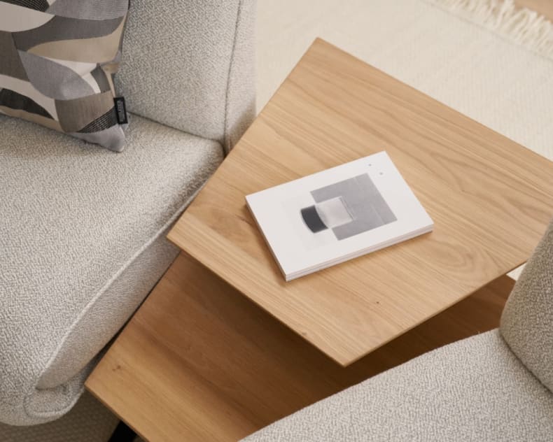 Ein Buch mit geometrischem Einband ruht auf einem Holztisch zwischen zwei Himolla Trapezsofa 4362 Loungesesseln mit hellen Polstern.