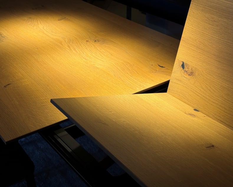 Das Sonnenlicht beleuchtet die natürliche Maserung und die dunklen Äste der schrägen Holzbretter des Girsberger Auszugstisches Bela und setzt warme Akzente.