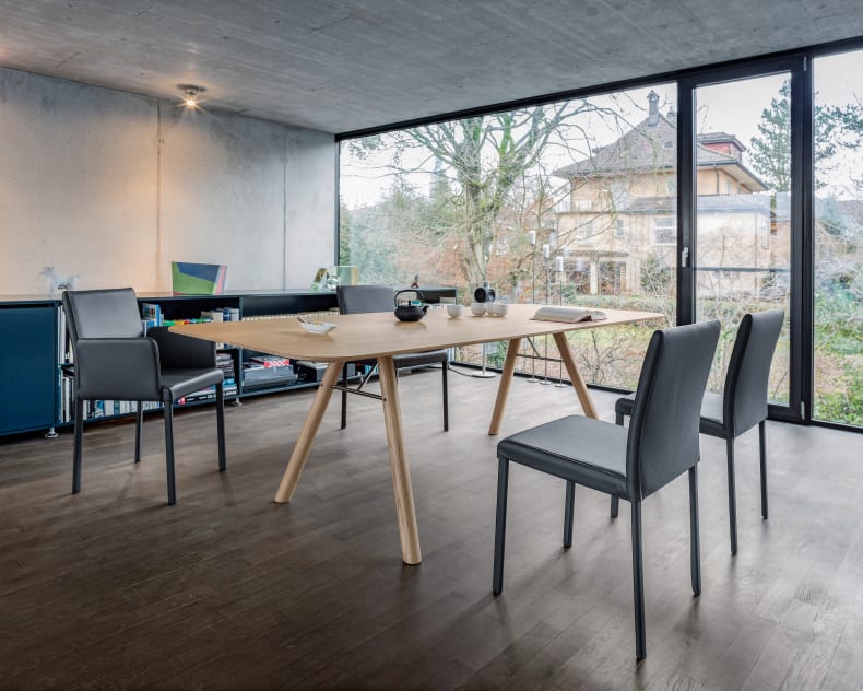 Das moderne Esszimmer ist mit einem Holztisch, sechs Girsberger Stuhl Kuba und großen Fenstern ausgestattet, die den Blick auf Bäume und ein Nachbarhaus freigeben.