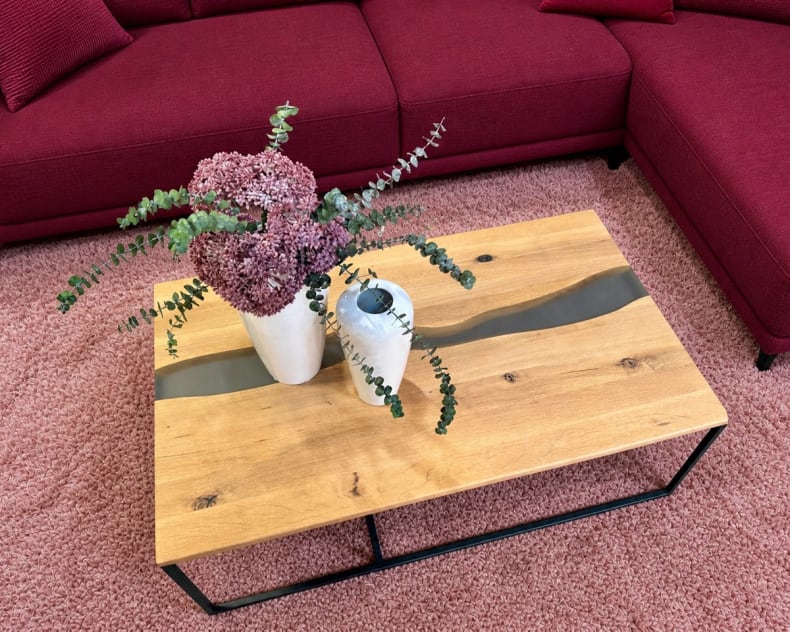 Ein hölzerner Couchtisch mit zwei Vasen, eine davon mit Blumen, auf einem rosa Teppich neben einem roten Sektionssofa.