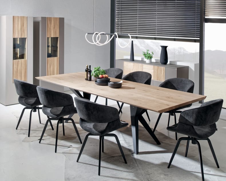 Modernes Esszimmer mit dem Voglauer Lacera Tisch, acht schwarzen Stühlen und minimalistischem Dekor in der Nähe großer Fenster.