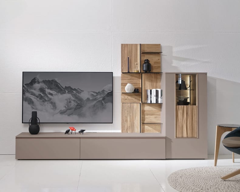 Modernes Wohnzimmer mit dem Voglauer Wohnmöbel Lacera: ein schlichter Schrank mit einem an der Wand befestigten Fernseher, stilvollen Regalen, Büchern und dekorativen Vasen.