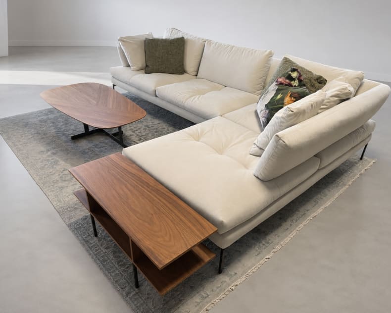 Das Bonaldo Sofa Aliante in Beige, gepaart mit dekorativen Kissen, zwei Couchtischen aus Holz und einem Teppich auf einem hellen Boden.