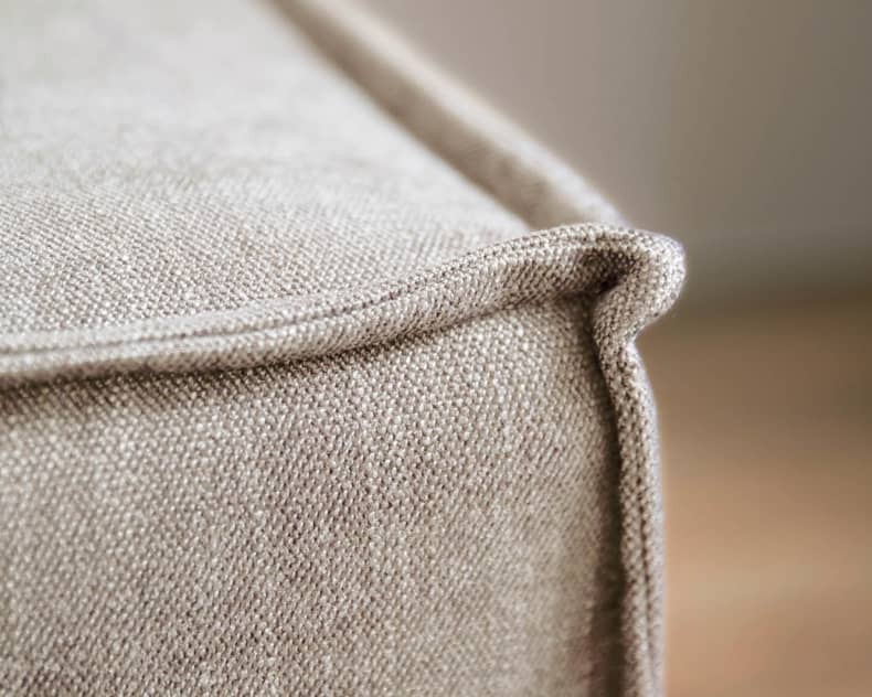 Nahaufnahme der Sofaecke Utica aus beigem Stoff mit engen Nähten und glatter Textur.