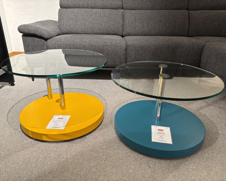Deux guéridons à plateau en verre et piètement jaune et bleu sont disposés sur un tapis gris devant un canapé gris. Produit : Mobilier de bureau avec 3 jardinières.