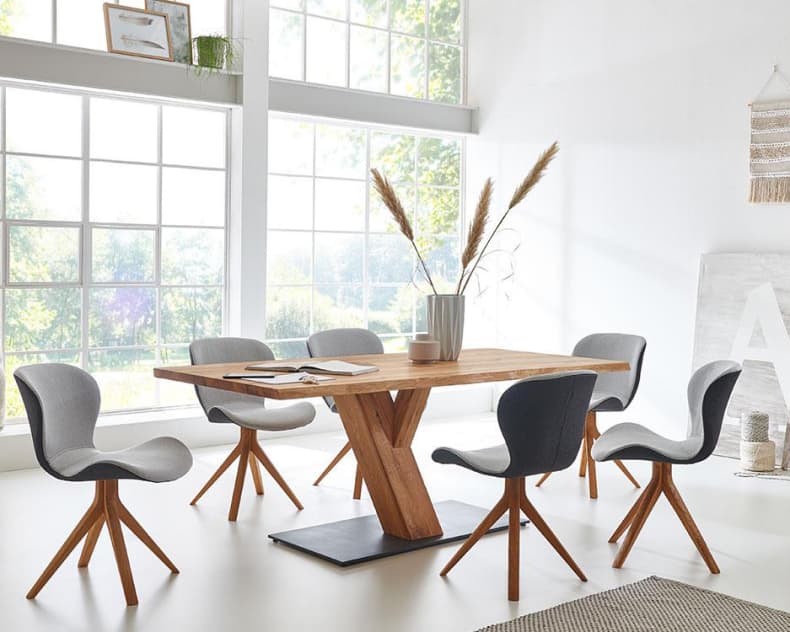 Ein modernes Esszimmer mit dem Holztisch Wimmer Säulentisch Zweigl Z30, ergänzt durch graue Stühle, große Fenster und eine Vase mit hohem Gras auf dem Tisch.
