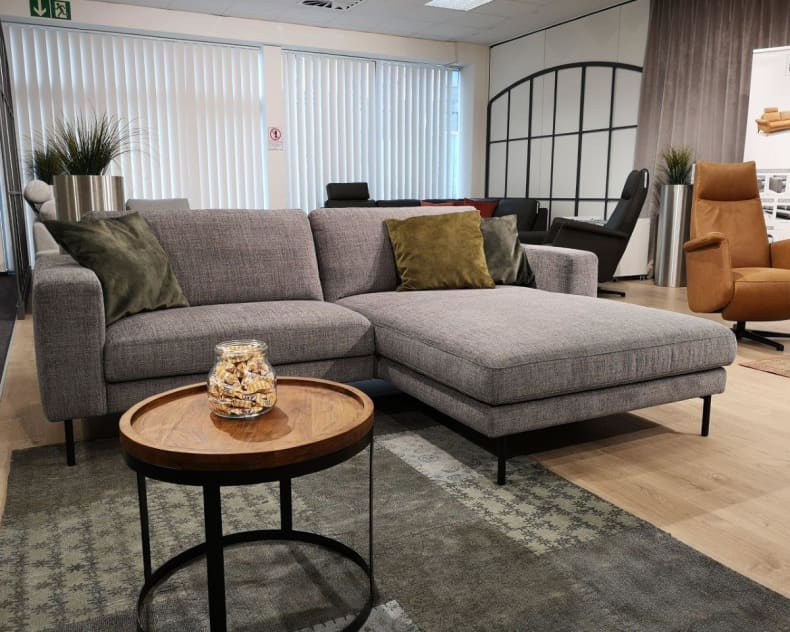 Modernes Wohnzimmer mit dem grauen Sektionssofa Polstergruppe Living, ergänzt durch einen runden Couchtisch aus Holz und stilvolle Dekokissen.