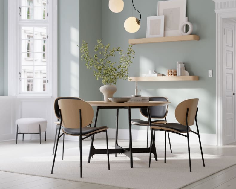 Modernes Esszimmer mit dem runden Tisch Dan Form Tisch Ooid, vier Stühlen, grünen Wänden, Regalen und einer Vase mit Zweigen.
