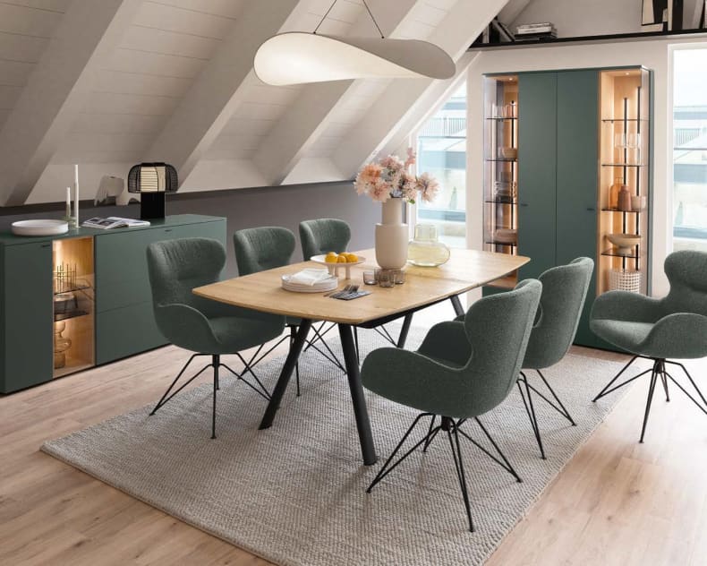 Modernes Esszimmer eingerichtet mit dem Venjakob Wohnprogramm Vanya: Holztisch, sechs grüne Stühle, Sideboard, Schränke und stilvolles Dekor.