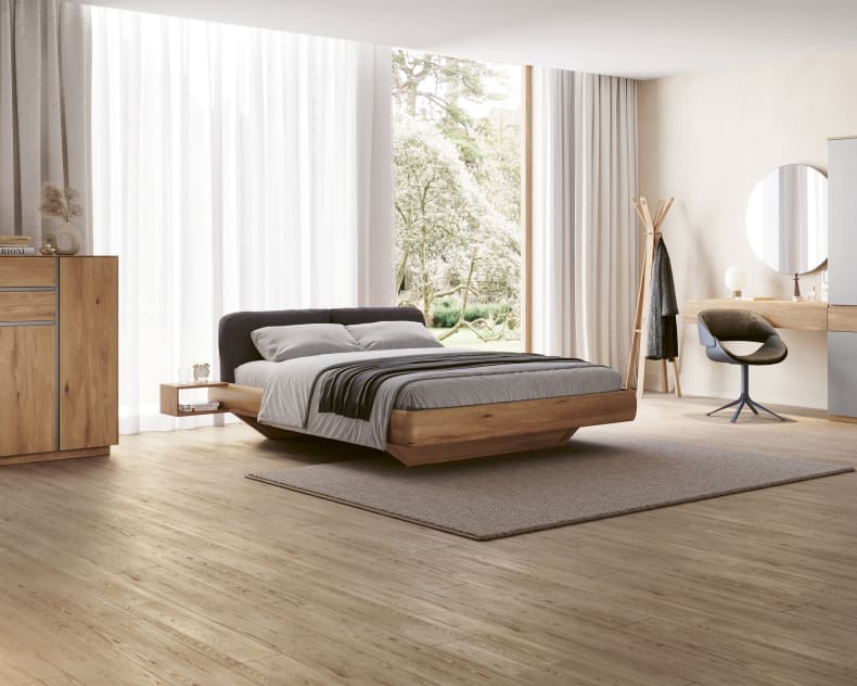 Minimalistisches Schlafzimmer mit dem Schwebebett Wimmer Bett Silvan, großen Fenstern, Holzfußboden und modernen Möbeln.