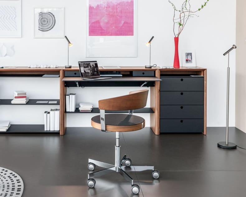 Modernes, minimalistisches Büro mit dem Girsberger Sideboard LaPunt, einem Holzschreibtisch, Drehstuhl, Laptop, Büchern, Wandkunst und einer hohen Vase mit Zweigen.