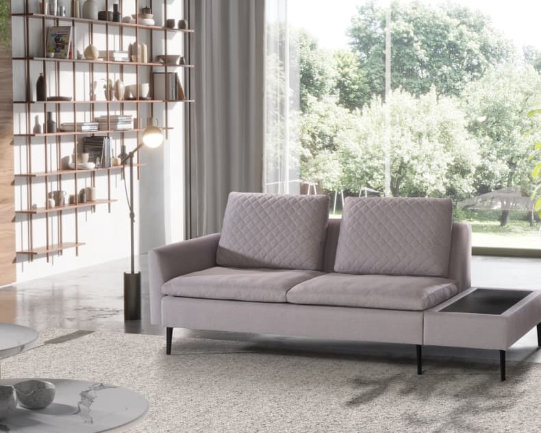 Modernes Wohnzimmer mit dem Artanova Sofa Dyo 9192 in Hellgrau, mit einem großen Fenster, Bücherregalen und einem malerischen Blick ins Grüne.