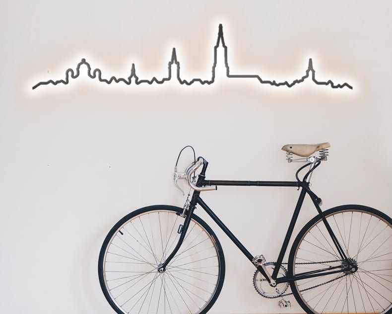Ein schwarzes Velo lehnt an einer weissen Wand, gekrönt vom beleuchteten Kontura City Bern Skyline Dekor.