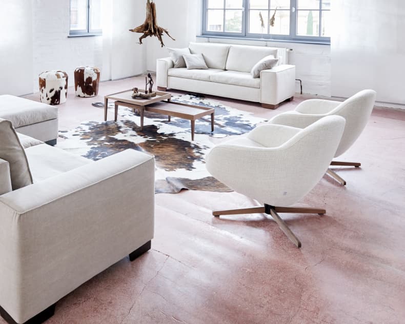 Modernes Wohnzimmer mit Signet Sessel Messina Jester klein, leichten Sofas, Kuhfellteppich, Couchtisch und großen Fenstern.
