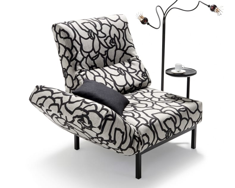 Das Signet-Sofa Chimba ist mit einem auffälligen schwarzen Blumenmuster versehen und wird von einem Beistelltisch mit einer Tasse und einer einzigartigen Lampe mit drei Glühbirnen begleitet.