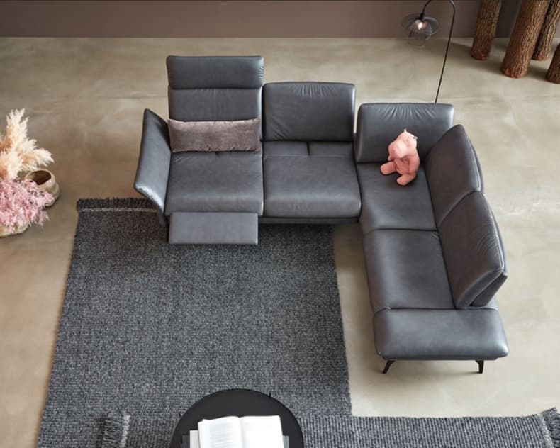 Ein Himolla Sofa Promotion 1928 in Grau, geschmückt mit einem rosa Teddybär und einem Kissen, steht auf einem Teppich in einem stilvollen Wohnzimmer.