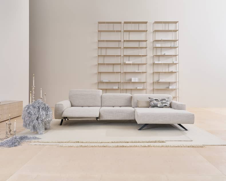 Modernes minimalistisches Wohnzimmer mit dem Himolla Sofa Signa 1552 in Hellgrau, ergänzt durch Regale und minimale dekorative Akzente.