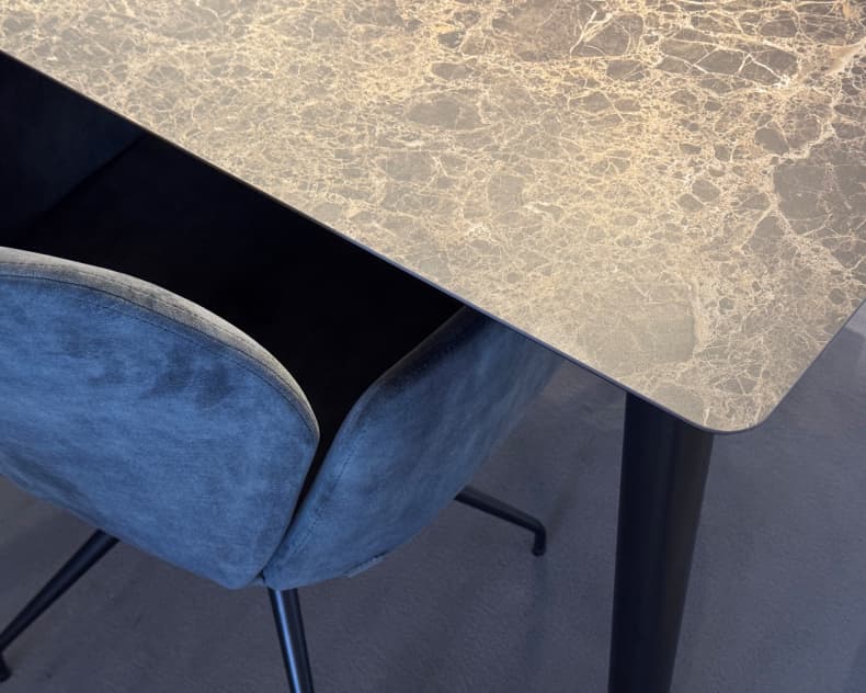 Der Mobitec Tisch Terra T0300 mit Marmorplatte steht zusammen mit einem dunklen Sessel aus Samt auf einem grauen Boden, schräg von oben gesehen.