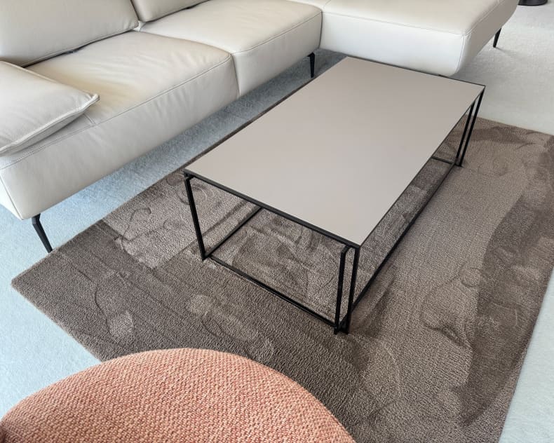 Der Bacher Couchtisch Minero steht auf einem strukturierten Teppich neben einem weißen Sofa und einem rosa Sessel in einem hellen Wohnzimmer.