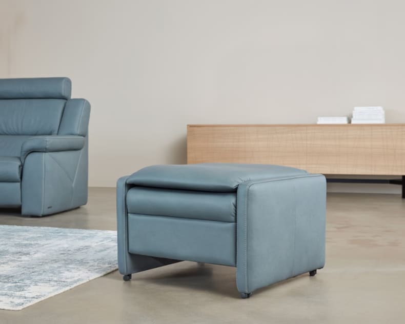 Der Himolla Einzelhocker/Sessel 7112 in blauem Leder ist in einem modernen Wohnzimmer zu sehen, zusammen mit einem passenden Sofa und einem Holzsideboard im Hintergrund.