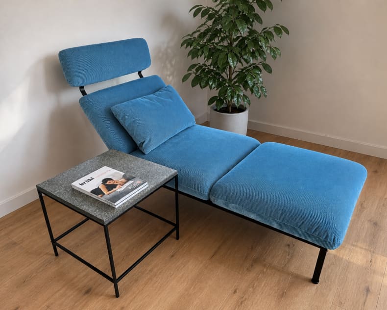 Die blaue Chaiselongue Liege Roro 98 steht neben einem kleinen Beistelltisch mit einer Zeitschrift, neben einer Topfpflanze auf einem Holzboden.