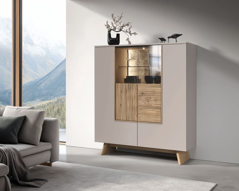 Das Voglauer Sideboard Lacera mit seinen Holz- und Glastüren wird in einem hellen Wohnzimmer mit Vasen und Skulpturen geschmückt.