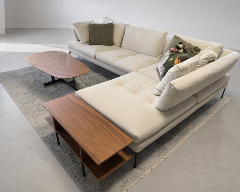 Das Bonaldo Sofa Aliante in Beige, gepaart mit dekorativen Kissen, zwei Couchtischen aus Holz und einem Teppich auf einem hellen Boden.