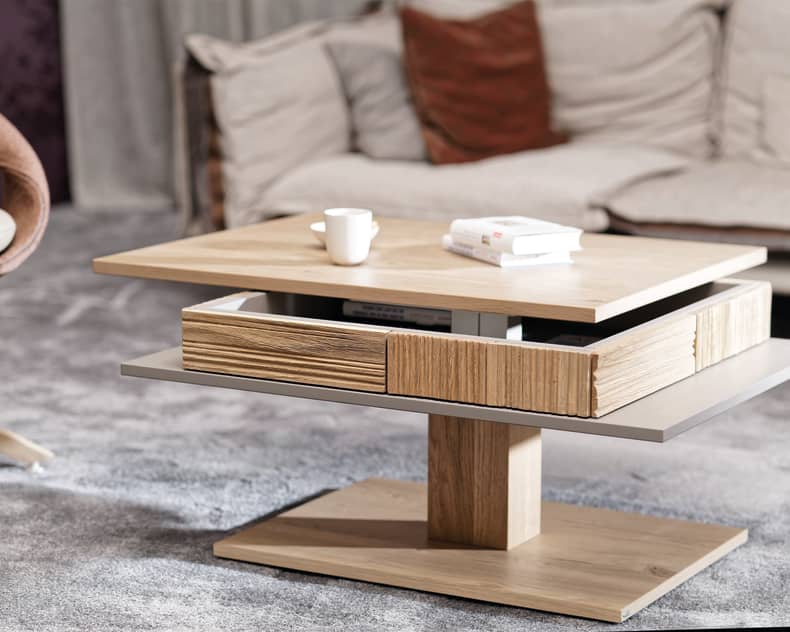 Der Voglauer Salontisch LAC77 ist ein moderner Couchtisch aus Holz mit drehbaren Etagen, auf dem Bücher und eine Tasse in einem gemütlichen Wohnzimmer stehen.