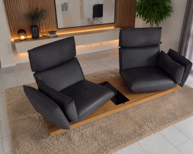 Das Koinor Sofa Experio, bestehend aus zwei modernen schwarzen Sesseln auf einem Holzgestell, wird in einem stilvollen Wohnzimmer auf einem beigen Teppich in Szene gesetzt.