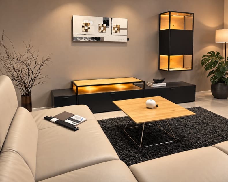 Modernes Wohnzimmer mit der beleuchteten Wohnwand „Plan X6“ von Venjakob, ergänzt durch ein beiges Sofa, einen Couchtisch aus Holz und einen schwarzen Teppich.