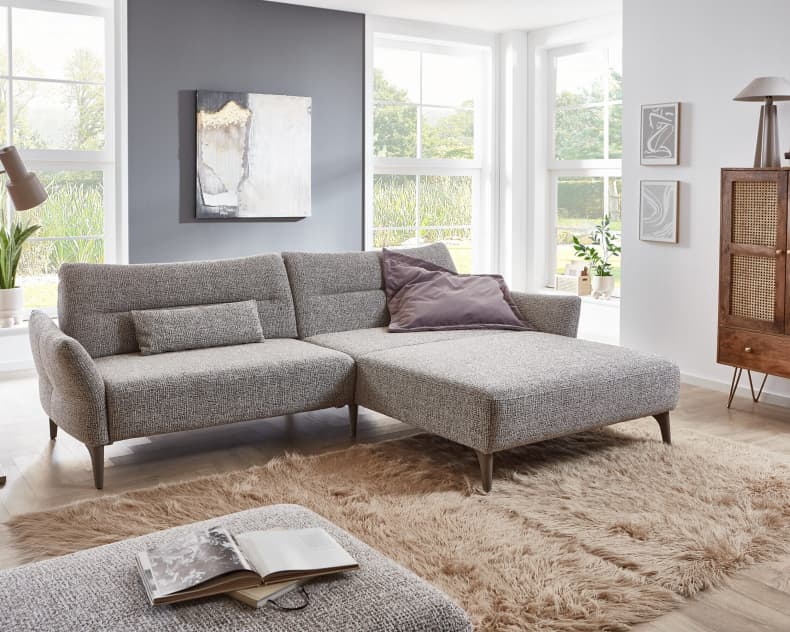 Modernes Wohnzimmer mit dem Ponsel Sofa Paula, einem stilvollen grauen Sektionssofa, gepaart mit einem weichen Teppich, großen Fenstern und elegantem Dekor.