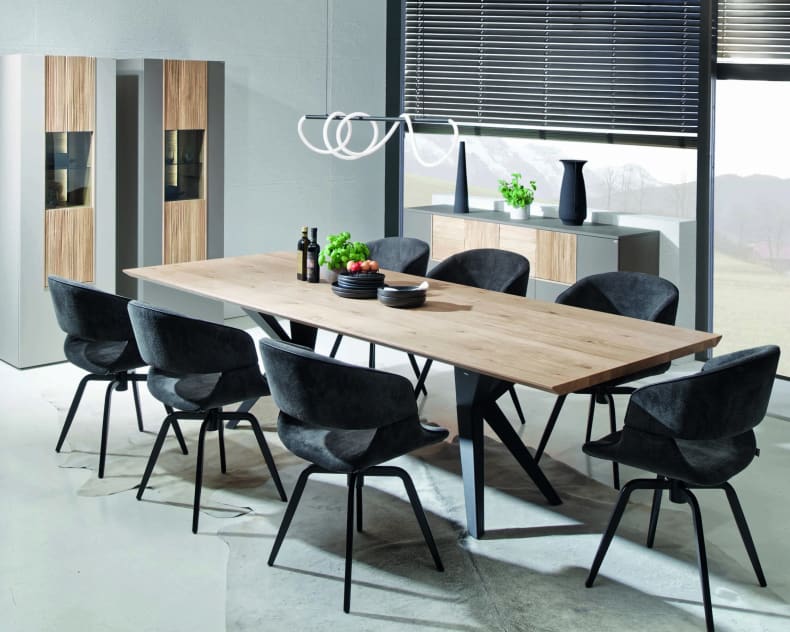 Modernes Esszimmer mit dem Voglauer Lacera Tisch, acht schwarzen Stühlen und minimalistischem Dekor in der Nähe großer Fenster.