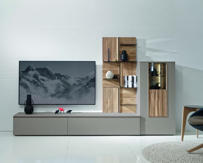 Modernes Wohnzimmer mit dem Voglauer Wohnmöbel Lacera: ein schlichter Schrank mit einem an der Wand befestigten Fernseher, stilvollen Regalen, Büchern und dekorativen Vasen.