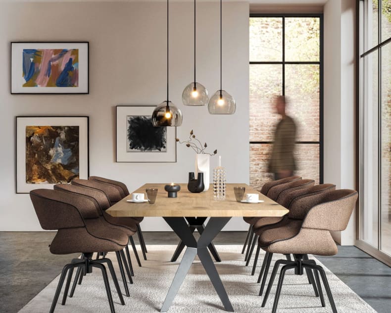 Salle à manger moderne avec une table en bois, huit chaises Voglauer Stuhl 74 en brun, des suspensions et une œuvre d'art murale abstraite.