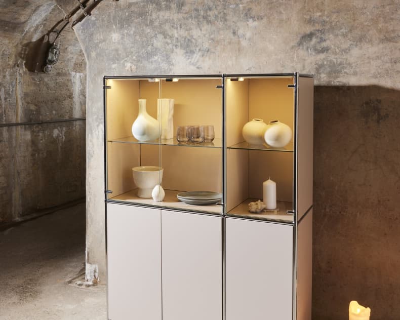 Helle Metallvitrine mit Glasböden, auf denen Vasen und Kerzen stehen.