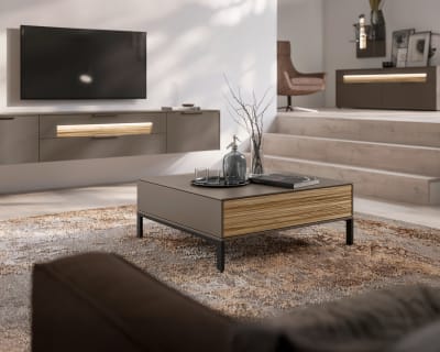 Modernes Wohnzimmer in neutralen Farbtönen, mit dem eleganten Couchtisch SALE 25 Wohnkombination Linee, TV-Set und gemütlicher Sitzecke.
