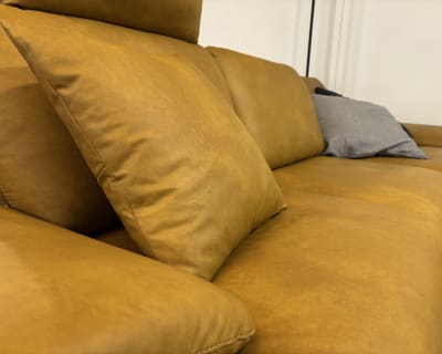 Gros plan du canapé jaune moutarde « Groupe de rembourrage Samiraa » avec des coussins moelleux, dont un gris, devant un mur blanc.
